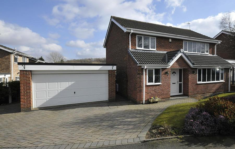 A white double-width garage door on a red brick house, set beneath a flat canopy with a block-paved driveway in front.